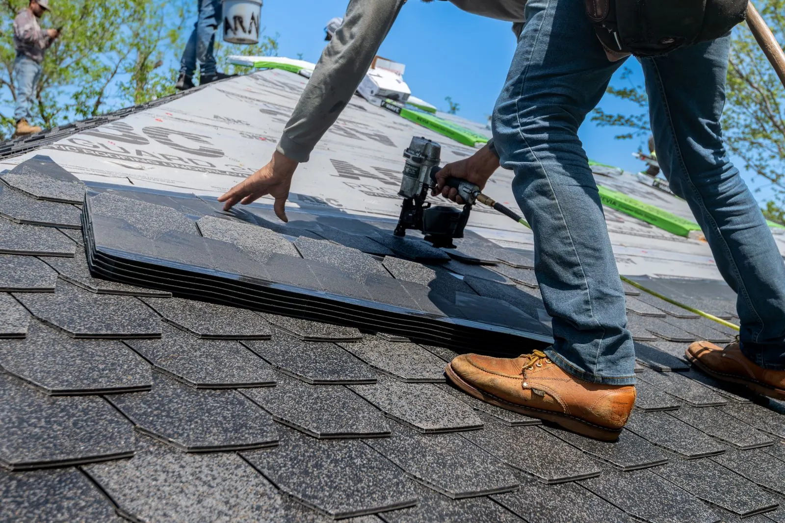Roofer nailing architectural shingles onto a new residential roof