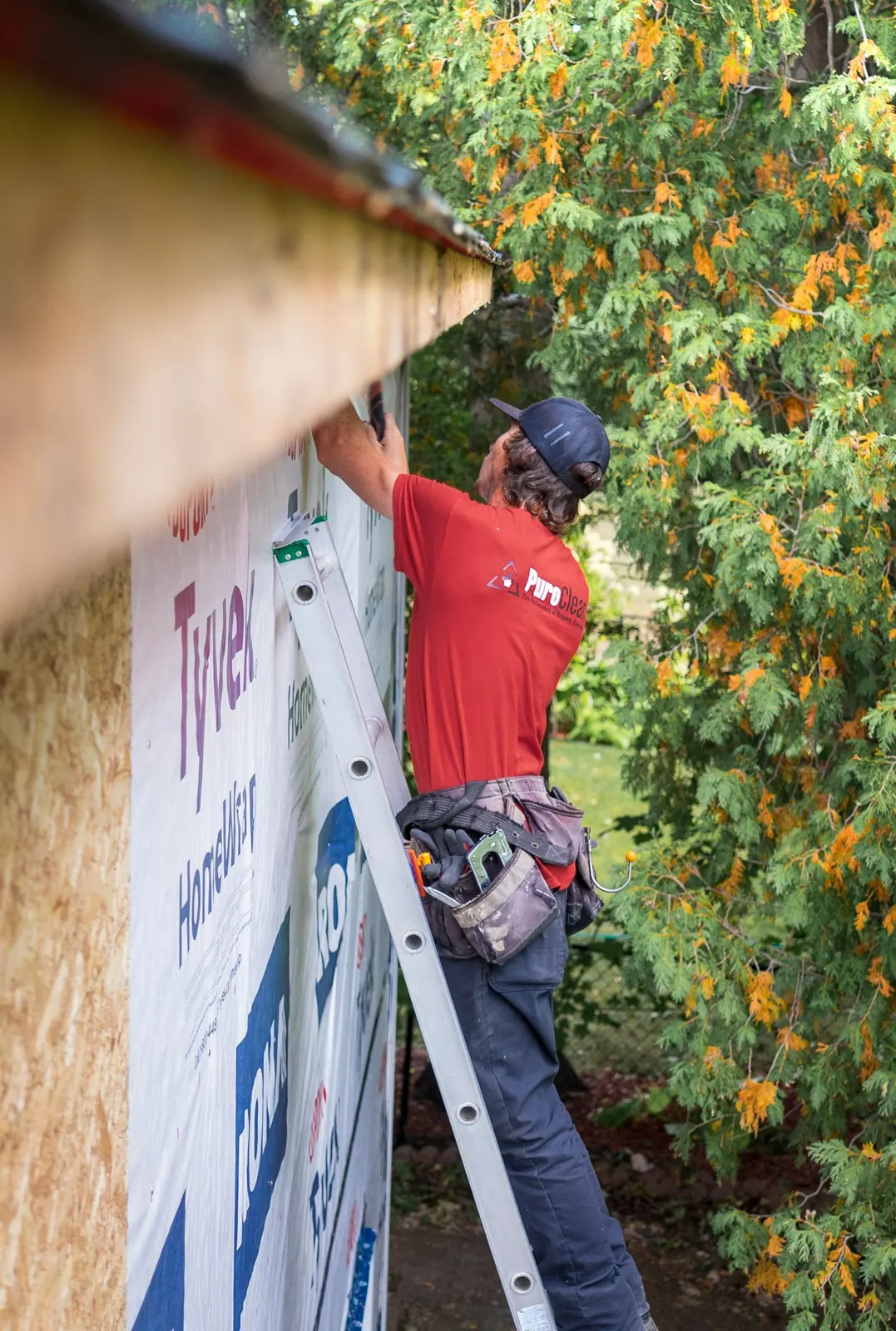 Installer fastening house wrap and siding from a ladder